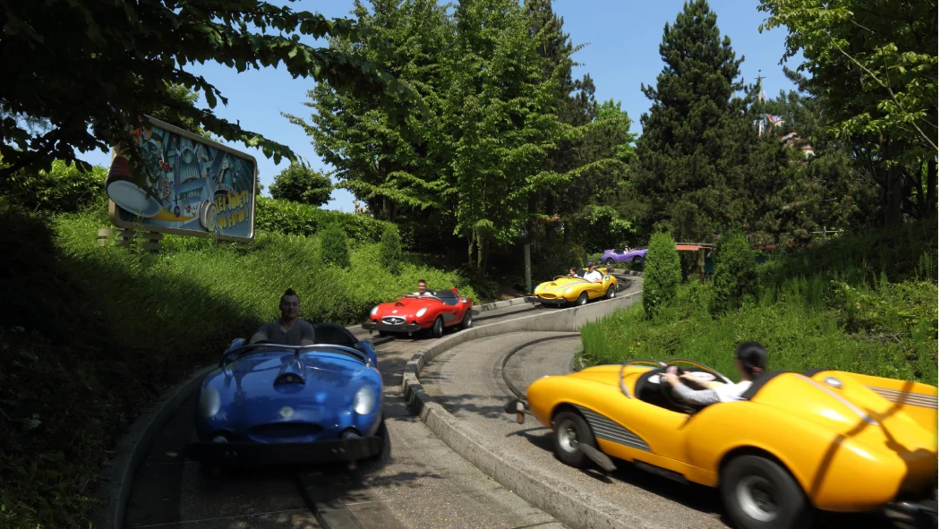 Guests driving colorful cars on the Autopia track surrounded by greenery at Disneyland Paris