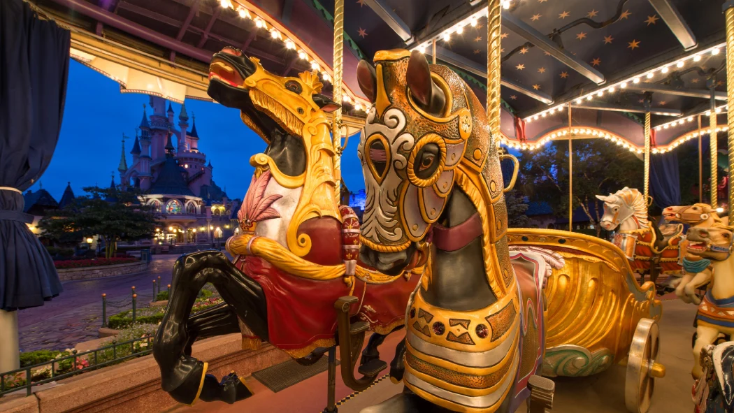 Close-up of ornate carousel horses with Sleeping Beauty Castle glowing in the background at night in Disneyland Paris