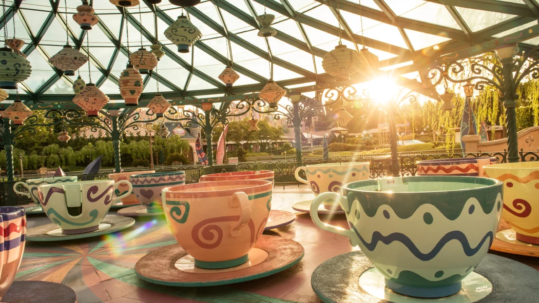Colorful spinning teacups of the Mad Hatter’s Tea Cups ride under a glass canopy at sunset in Disneyland Paris