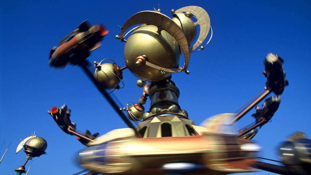 The Orbitron ride spinning futuristic rocket vehicles around golden planetary structures against a clear blue sky