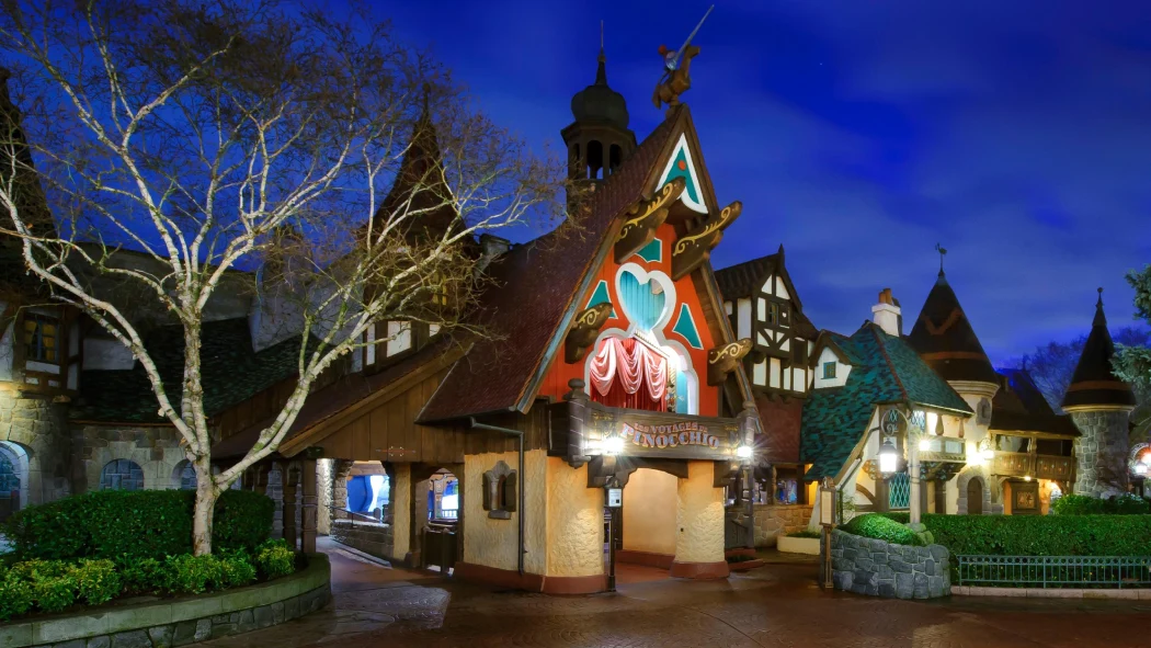 Exterior view of the Pinocchio’s Daring Journey ride with storybook-style architecture lit up in the evening
