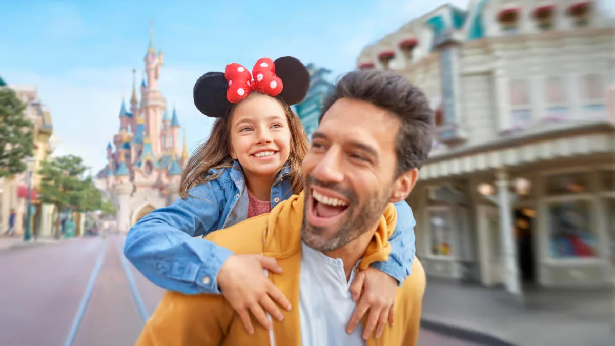 A father gives his daughter a piggyback ride in Disneyland® Paris, both smiling happily in front of the park