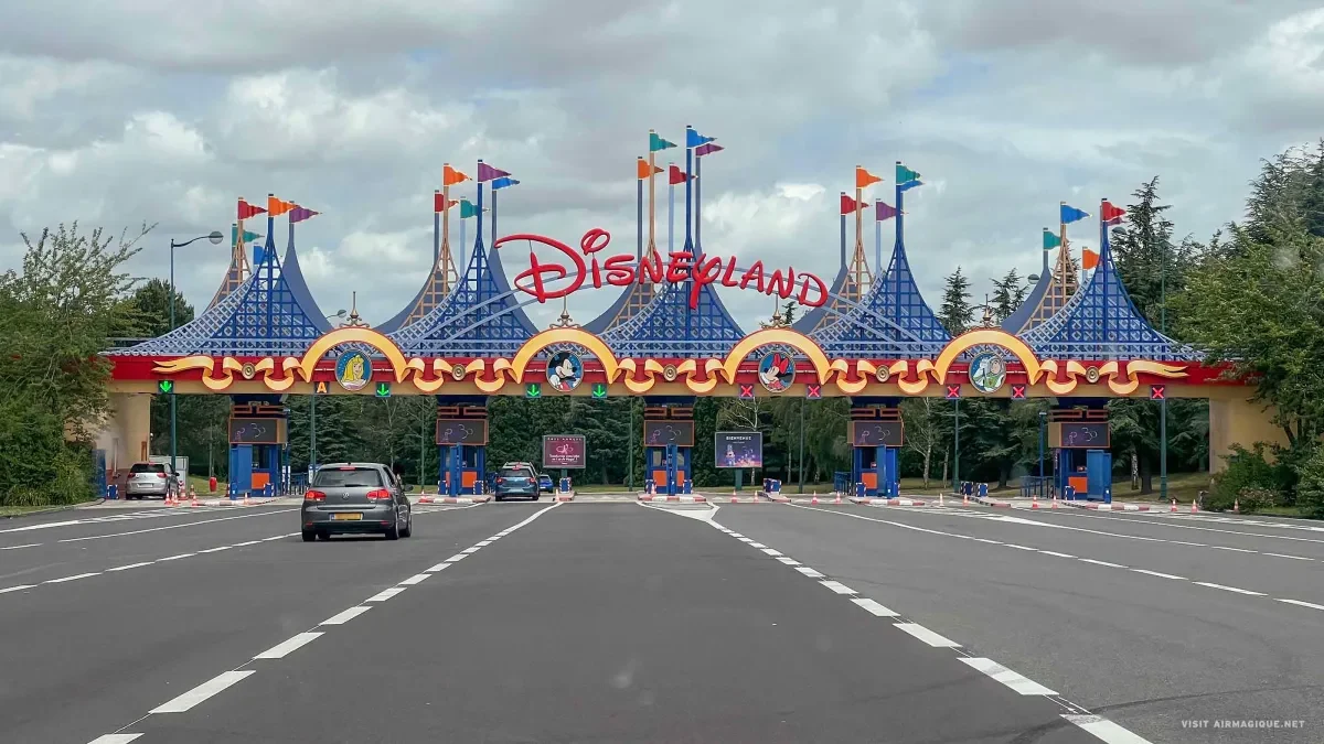 Cars drive through the colorful entrance gate of Disneyland Paris with the logo above