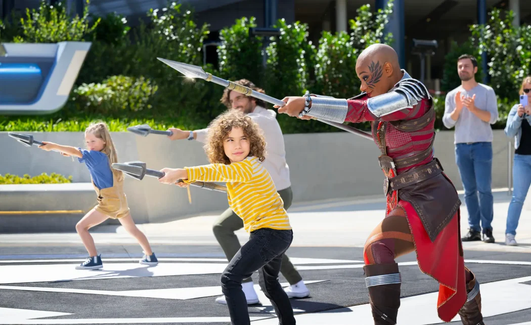 A child participates in an interactive Marvel experience, learning to throw spears with a character in Disneyland® Paris.