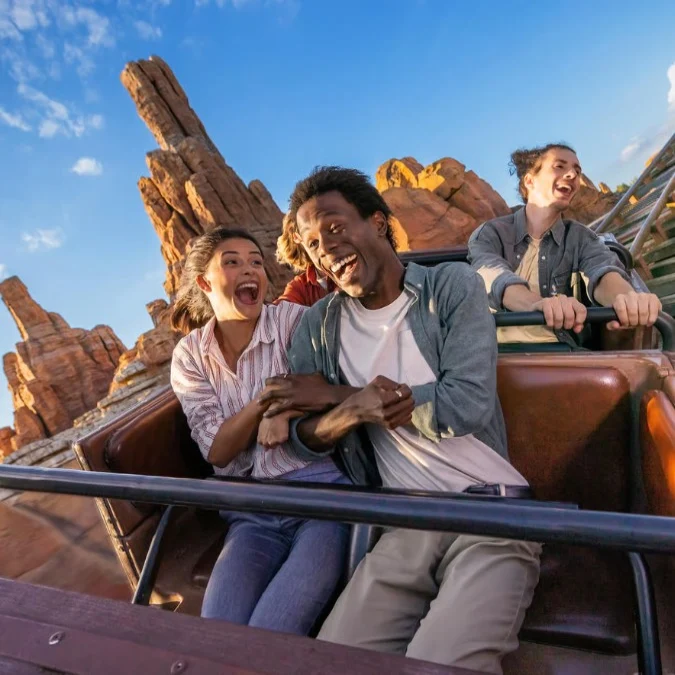 A group of friends enjoy a thrilling roller coaster ride at Disneyland® Paris, smiling and laughing in excitement