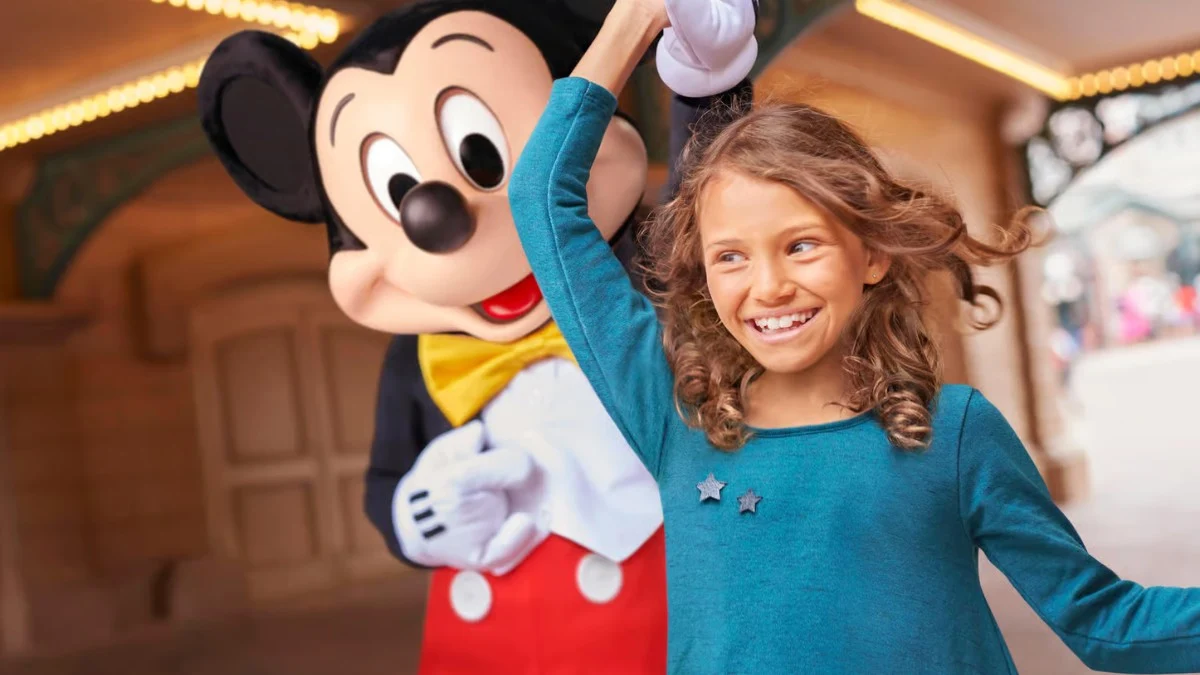 Smiling girl twirls with Mickey Mouse at a Disney park