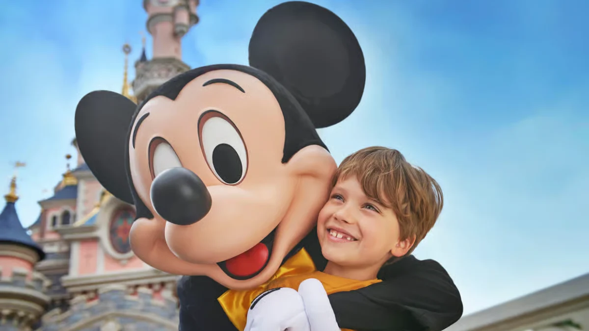 mickey-mouse-hug-child-disneyland Mickey Mouse hugs a smiling boy in front of the Disneyland Paris castle